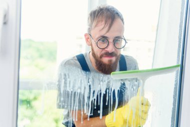 Profesyonel bir temizlikçi olarak mavi üniformalı bir adam pencereyi lastik fırçayla yıkıyor.