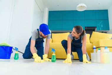 Gülümseyen kız ve yakışıklı sakallı adam temizlik öğeleri ile parke yıkama ve paçavra ile wipping workwears