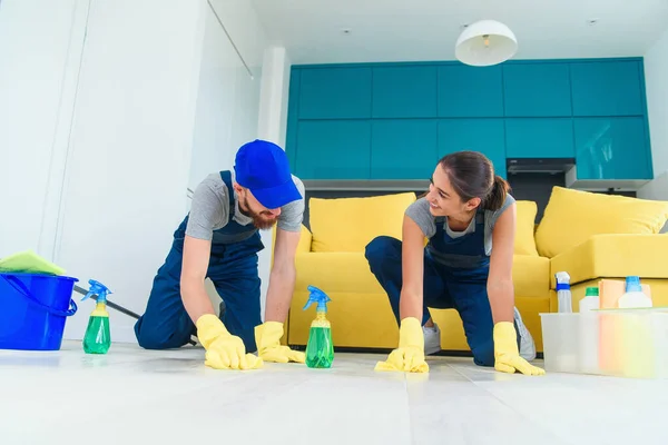 Smiling girl and handsome bearded man in workwear washing the parquet with the cleaning items and wipping with rags — Stok Foto