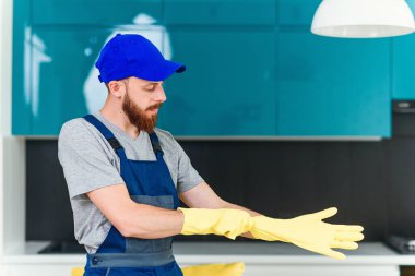 Temizlik hizmeti nden bakımlı sakallı çekici adam iç mutfağı temizlemek için koruyucu lastik eldiven giyiyor