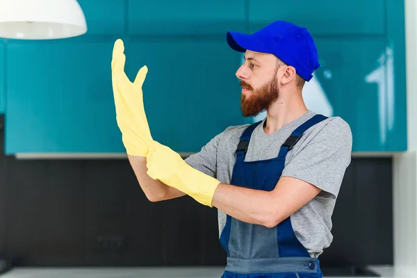 Ελκυστικός τύπος με καλά καλλωπισμένο μούσι από την υπηρεσία καθαρισμού φορώντας προστατευτικά λαστιχένια γάντια για να καθαρίσετε την εγχώρια κουζίνα — Φωτογραφία Αρχείου