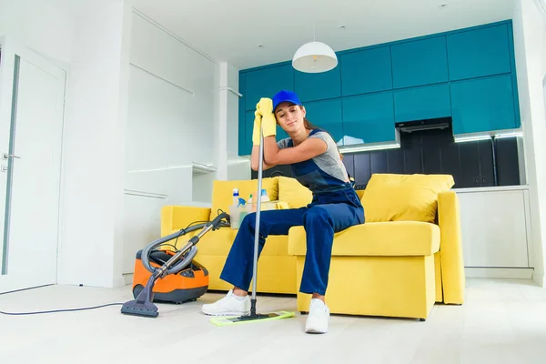 Pretty housewife tired of cleaning sits on the couch and leans to the mop after finish washing the floor. — Stock Photo, Image