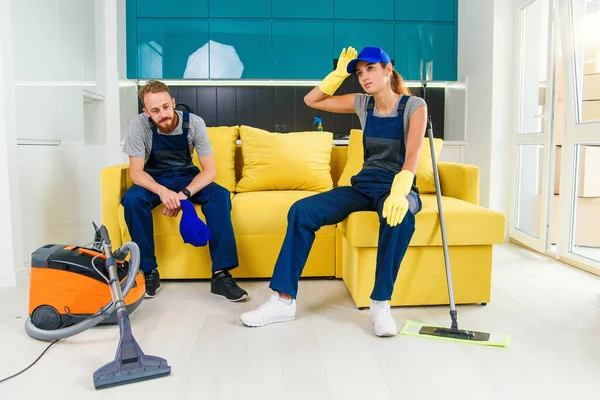 Happy couple of professional cleaners having rest in sofa after cleaning cuisine.