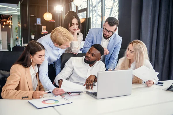 Razas mixtas corporativas jóvenes compañeros de trabajo que discuten la estrategia de negocio de su empresa exitosa utilizando el ordenador portátil en la mesa de la sala de juntas . — Foto de Stock