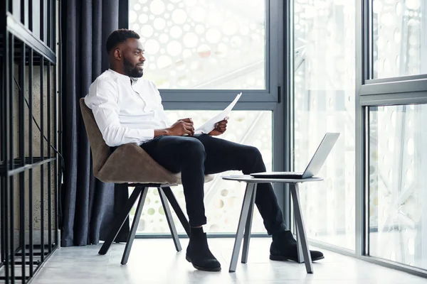 Hombre de negocios afroamericano guapo que trabaja en la computadora portátil y el análisis en la habitación especialmente designada en la oficina moderna y elegante . — Foto de Stock