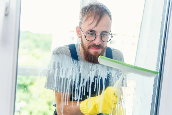 Ελκυστικός νέος άντρας με γένια σε ειδικά γυαλιά καθαρίζοντας το παράθυρο με ειδικό εργαλείο — Φωτογραφία Αρχείου
