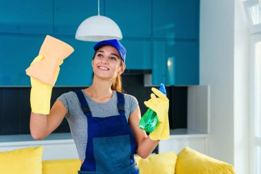 Koruyucu eldivenli genç bir kadın evini temizlerken sprey ve bez kullanıyor. Ev işi ve ev temizliği kavramı.