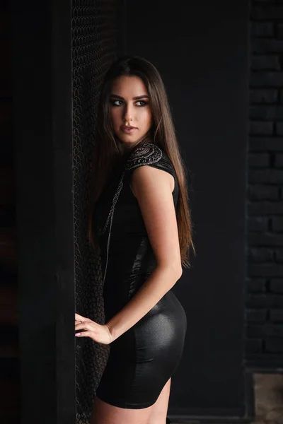 Urban stylish girl in sexual leather dress near metal grid. — Stock Photo, Image