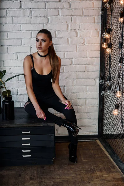 Hermosa mujer de moda en la habitación de estilo loft con pared de ladrillos blancos y red de hierro negro. Muchacha atractiva con figura perfecta en ropa negra con estilo . — Foto de Stock