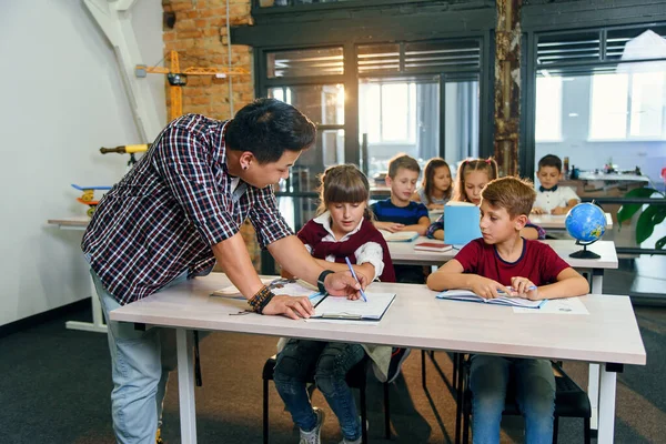 Los alumnos se sientan en los escritorios y escuchan al maestro mientras él explica el tema de la nueva lección . — Foto de Stock