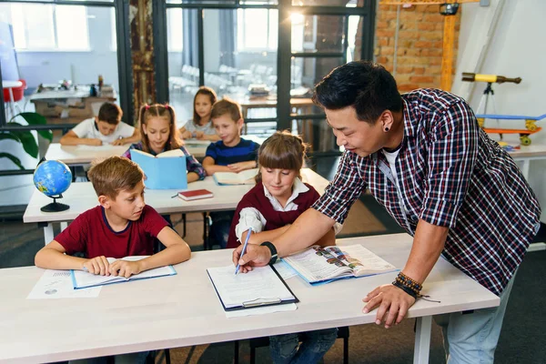 Los alumnos se sientan en los escritorios y escuchan al maestro mientras él explica el tema de la nueva lección . — Foto de Stock