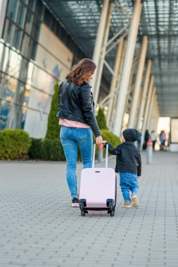 Güzel anne ve şirin kızı birlikte yürürler ve havaalanına pembe bir bavul çekerler..