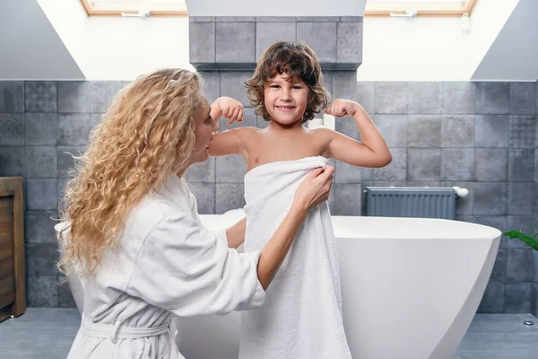 Прекрасна молода мати зі своїм гарним сином в сучасному стильному одязі в ванній і білому рушнику . — стокове фото