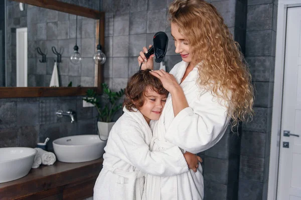 Mãe e filho se divertem juntos na casa de banho. Bela mãe com seu filho vestido de roupão de banho são relaxantes e brincando no banheiro juntos . — Fotografia de Stock