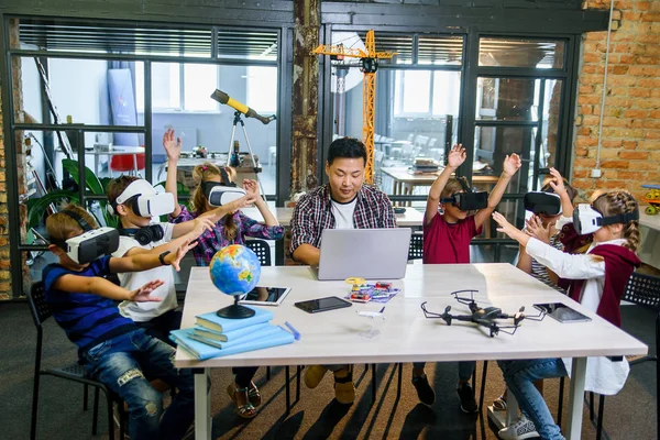 Grupo de jóvenes alumnos de primaria que utilizan gafas de realidad virtual durante la clase de codificación por ordenador . — Foto de Stock