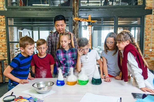 Ung manlig lärare förklarar för eleverna förångningsreaktion med färgat vatten och torr is i kemisk lektion. — Stockfoto