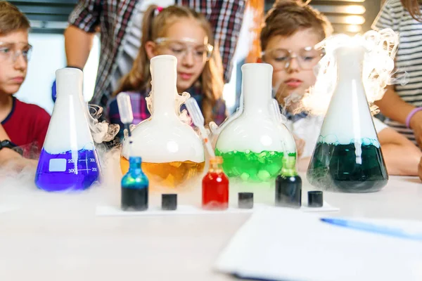 Kimya laboratuvarında bir grup beyaz öğrenci. Gözbebekleri, şişelere yoğun buharlaşmaya neden olan renkli sıvılarla kuru buz koyuyor.. — Stok fotoğraf