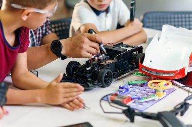 Akıllı okul laboratuvarında çalışan ve radyo kontrollü elektrikli araba modelini test eden Avrupalı okul çocuklarıyla birlikte erkek elektronik mühendisi..