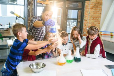 İlgilenen öğrenciler, cam şişelerdeki renkli sıvıların değişiminin kimyasal reaksiyonlarını inceliyor..