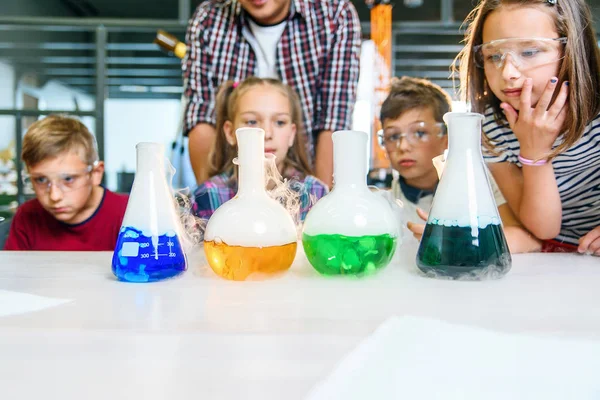 Güvenlik gözlüklü sevimli okul çocukları mataralarda renkli sıvılarla kimyasal deney yapıyorlar.. — Stok fotoğraf