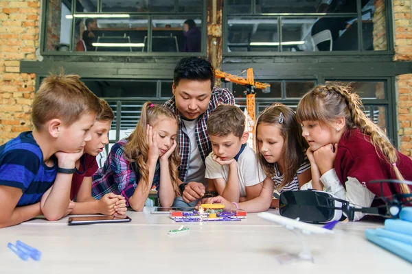 Los escolares inteligentes con maestro asiático investigan constructor electrónico con ventilador giratorio y bombilla. Alumnos creativos con científicos que trabajan en el proyecto tecnológico en la escuela . — Foto de Stock