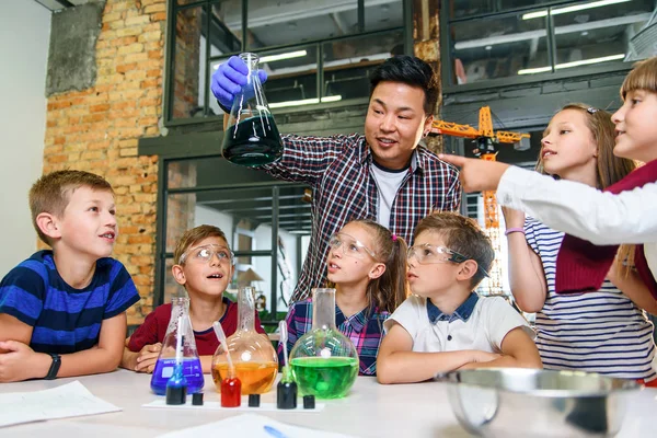 İlkokul öğrencileri, cam parçalarında renkli sıvılarla ilgili ilginç kimyasal deneyler yapan öğretmenlerini dikkatle izliyorlar.. — Stok fotoğraf