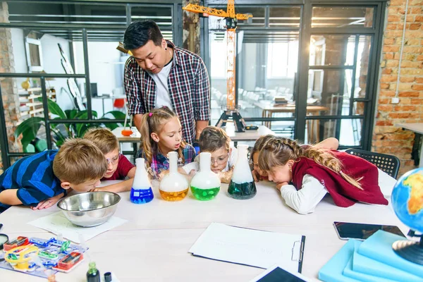 Caucasian school children in chemical lab. Pupils put dry ice into the flasks with colored liquids which causes intensive vaporization. Science, chemical reaction and educational concept.