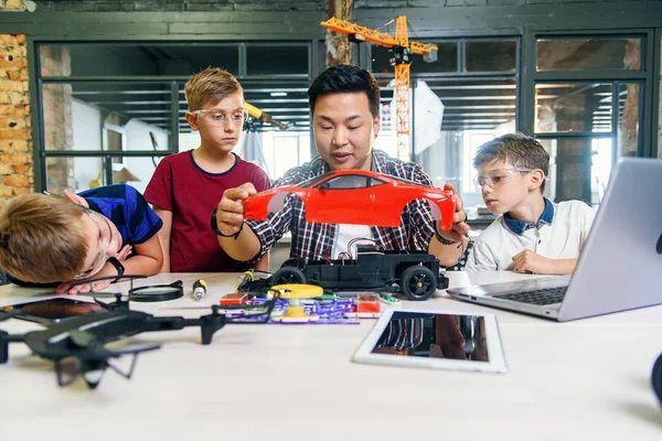 Young Korean man of electronics engineer with young children using screwdriver to disassemble robotic machine at the table in the modern school. Slow motion