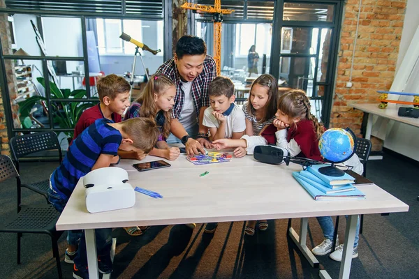 Clever school children with Asian male teacher investigate electronic constructor with turning fan and bulb. Creative pupils with scientist working on the tech project at school.