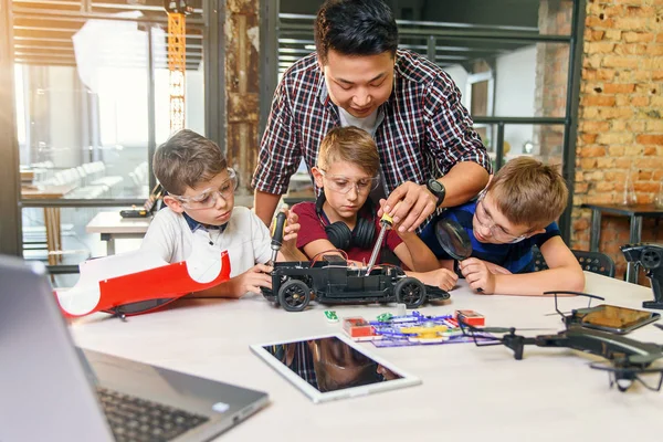 Ingeniero electrónico masculino con escolares europeos que trabajan en un laboratorio escolar inteligente y modelo de prueba de coche eléctrico controlado por radio . — Foto de Stock