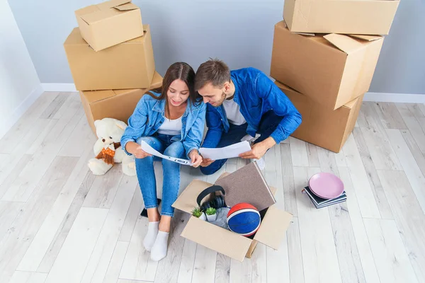 Pareja tienen una discusión sobre el diseño de su nuevo hogar sentado en el suelo de madera entre muchas cajas de cartón. Hermosa pareja joven y elegante en el amor planificación de diseño de la casa para su nuevo piso comprado . — Foto de Stock