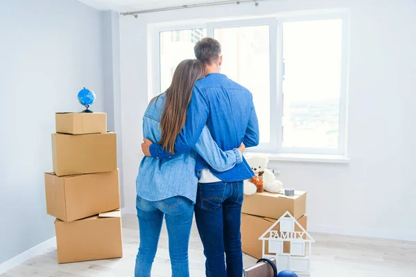 Cute couple in love looking out the window while standing together at their new home. — Stock Photo, Image