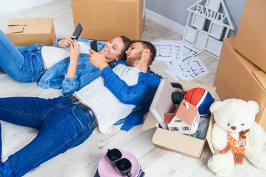 Yeni eve taşınırken ahşap zemine uzanan ve akıllı telefonlara mesaj atan mutlu beyaz çift..