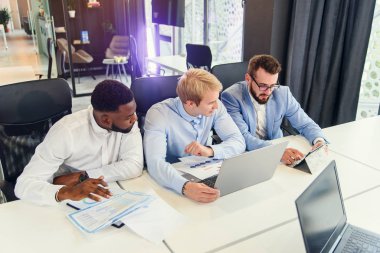 Üç melez ırk yakışıklı iş adamları iş stratejilerinin fırsatlarını bilgi içeren farklı raporlar kullanarak tartışıyor..