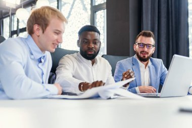 Ofis masasında oturan ve projelerini gözden geçirmek için bilgisayar kullanan kendine güvenen melez işadamları..