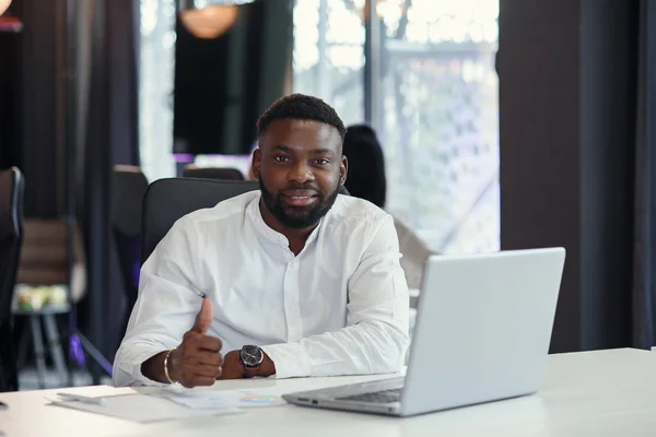 Tevreden Afrikaans-Amerikaanse office manager werkt op de laptop glimlachend en opgeheven duim. — Stockfoto