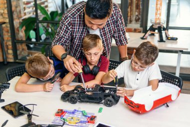 Akıllı okul laboratuvarında çalışan ve radyo kontrollü elektrikli araba modelini test eden Avrupalı okul çocuklarıyla birlikte erkek elektronik mühendisi..