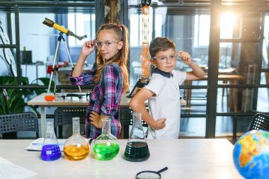 İlkokulda kollarını kavuşturup sırtüstü dururken sırtüstü gülümseyen koruyucu gözlüklü iki güzel öğrenci..