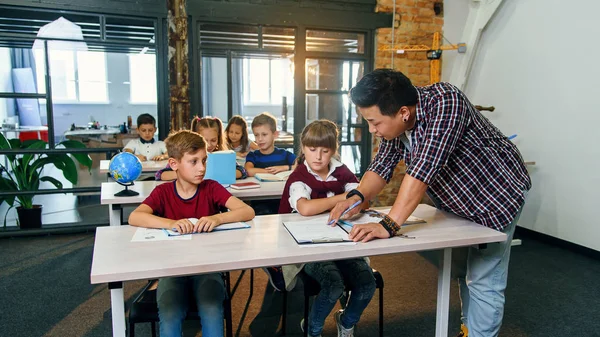 Profesor ayudando a escolares con tareas de prueba en el aula de la escuela primaria . — Foto de Stock