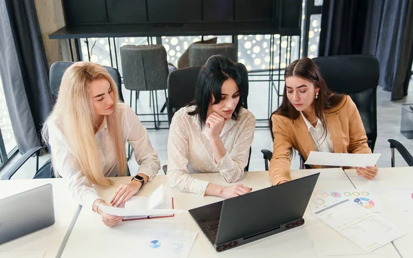 Jovenes trabajadoras de oficina sentadas en la sala de reuniones y discutiendo su proyecto de negocio conjunto usando datos financieros y computadoras . — Foto de Stock