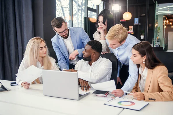 Razas mixtas corporativas jóvenes compañeros de trabajo que discuten la estrategia de negocio de su empresa exitosa utilizando el ordenador portátil en la mesa de la sala de juntas . — Foto de Stock