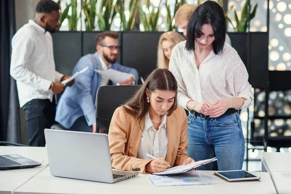 Zielstrebige Büroleiterin unterschreibt an ihrem Arbeitsplatz die Finanzunterlagen, die ihrer Sekretärinnen-Kollegin im Besprechungsraum übergeben werden. — Stockfoto