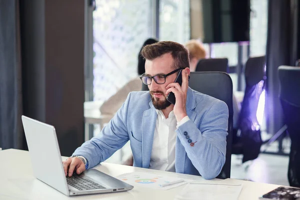 Professionele verkoopagent werkt op een laptop en adviseert mobiel met zijn zakenpartner in een modern samenwerkingscentrum. — Stockfoto