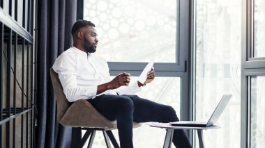 Laptopta çalışan yakışıklı Afro-Amerikan iş adamı ve modern şık ofisin özel olarak belirlenmiş odasında analizler yapıyor..
