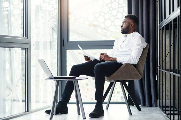 Hombre de negocios afroamericano guapo que trabaja en la computadora portátil y el análisis en la habitación especialmente designada en la oficina moderna y elegante . — Foto de Stock