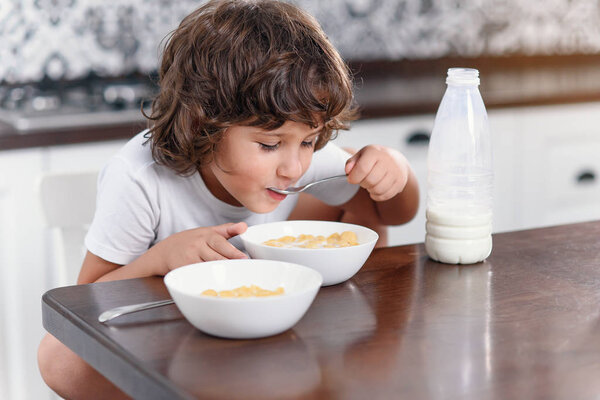 Счастливый маленький мальчик с удовольствием ест здоровый завтрак из кукурузных хлопьев и молока на кухне
.