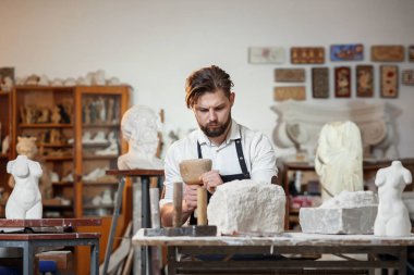 Sakallı zanaatkar bir keskiyle beyaz taş oymacılığında çalışıyor. Sanat eserleri ile yaratıcı atölye.