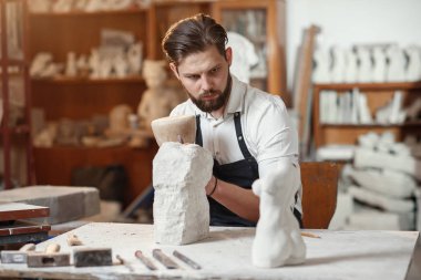 Beyaz gömlekli ve siyah önlüklü erkek heykeltıraş sanat stüdyosunda kadın gövdesinin kireçtaşından bir kopyasını yapıyor..