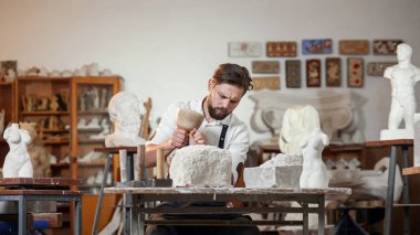 Sakallı zanaatkar bir keskiyle beyaz taş oymacılığında çalışıyor. Sanat eserleri ile yaratıcı atölye.