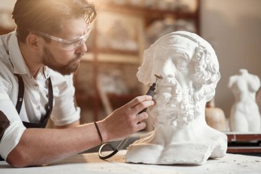 Erkek heykeltıraş, kadın heykelinin alçıtaşını tamir ediyor. Yaratıcı sanat stüdyosunun çalışma yerinde..